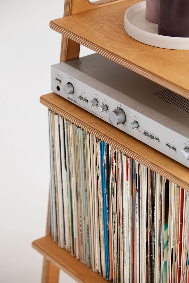 Close-up of amplifier resting above a full row of 12-inch LPs in the lower vinyl storage bay, wooden shelves