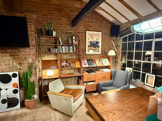 Wide view of custom teak plywood shelving and lounge area in a brick-walled London warehouse loft, designed by client Todd