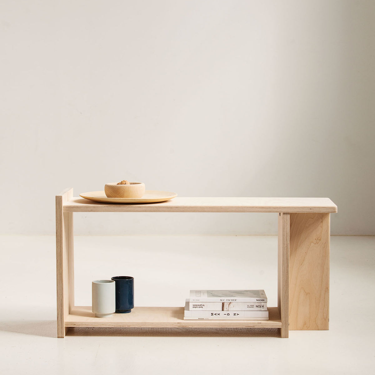 Minimalist wooden side table with a bowl, candle, and books on a plain background