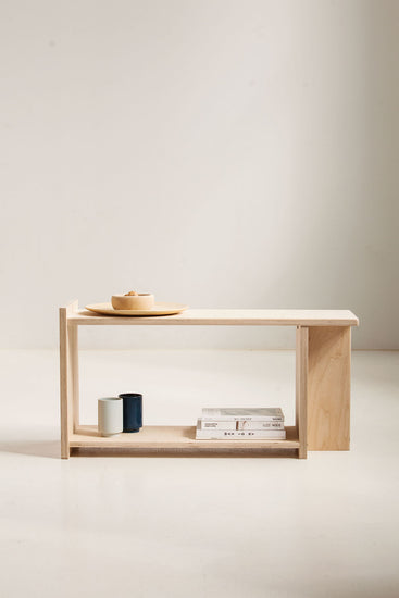 Minimalist wooden side table with a bowl, candle, and books on a plain background