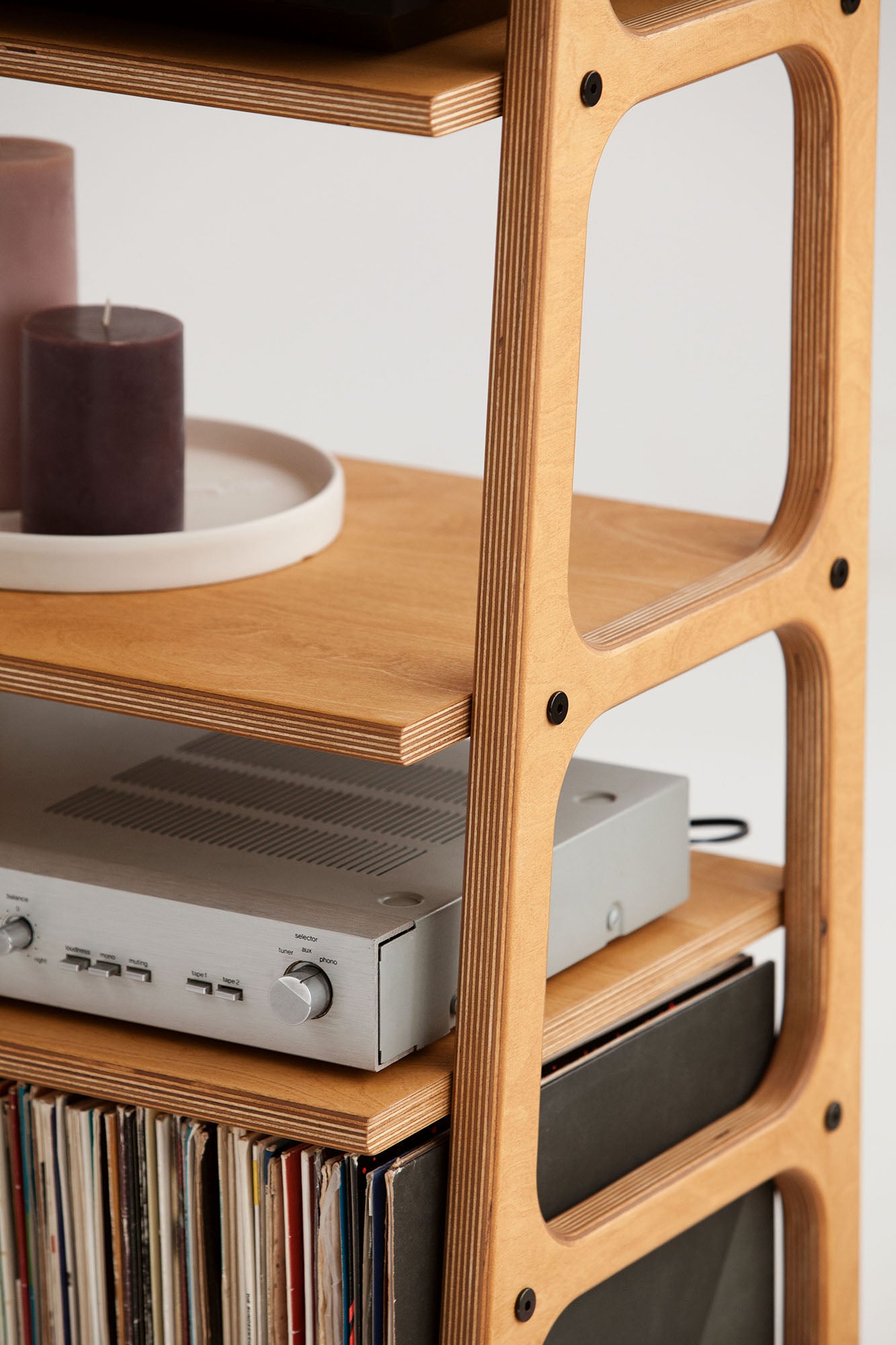 Detail of wooden ladder side legs of bookshelf with rounded cut-outs and shelf above the amplifier on the vinyl record stand.