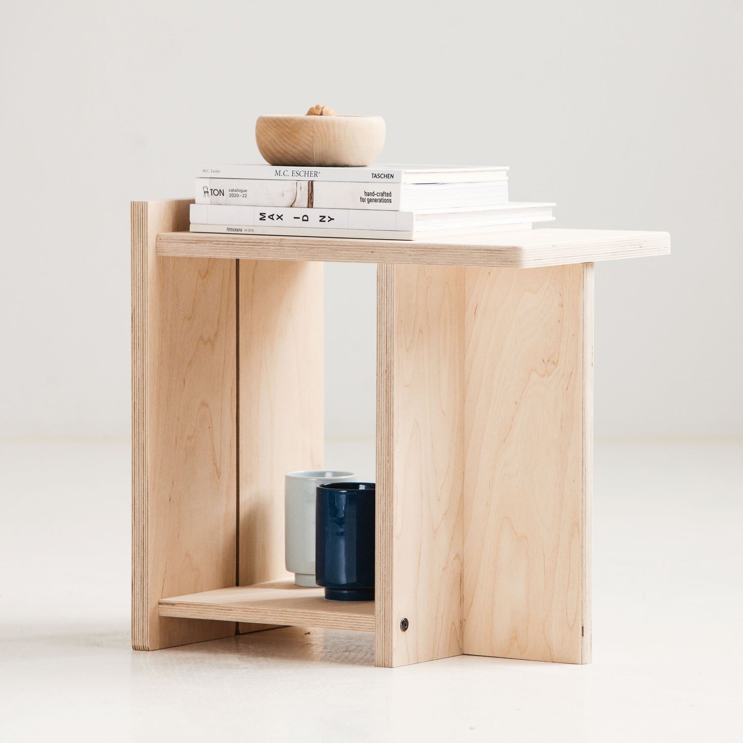 Wooden stool with a white top holding books and a bowl on a light gray background
