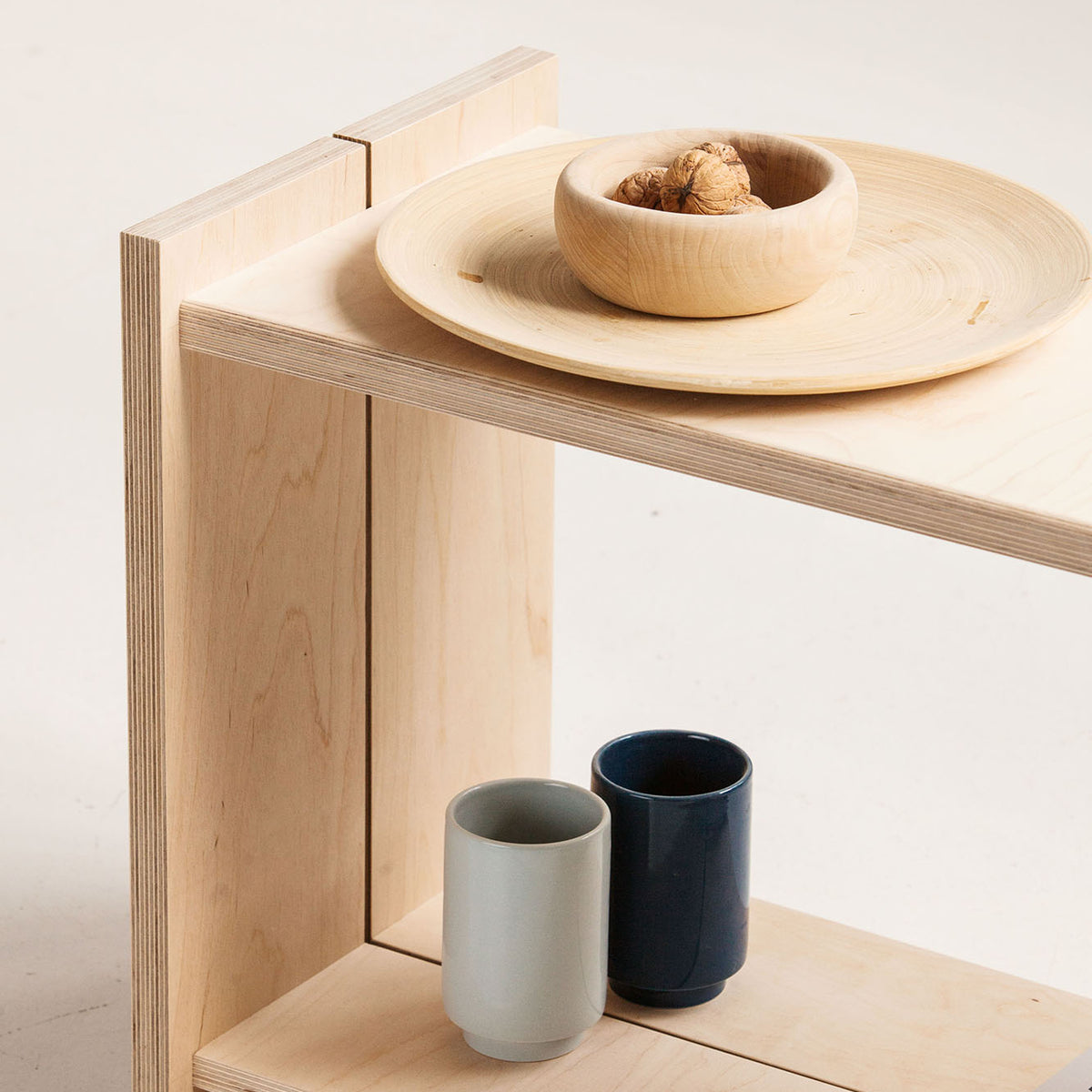 Wooden shelf with ceramic bowls and cups on a light background