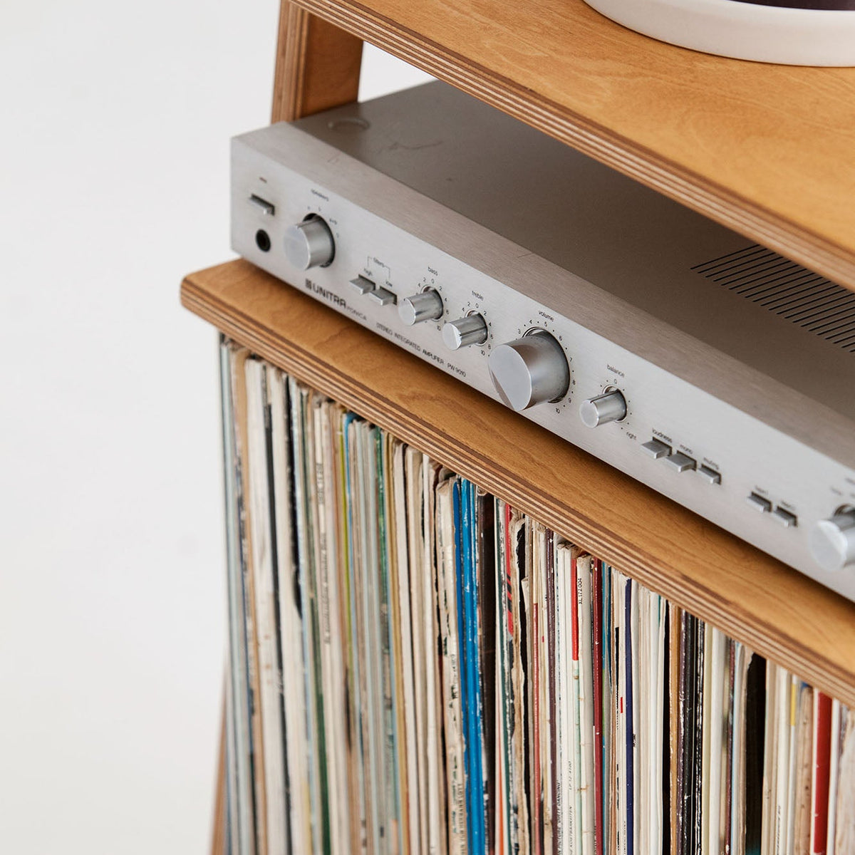Close-up of amplifier resting above a full row of 12-inch LPs in the lower vinyl storage bay, wooden shelves